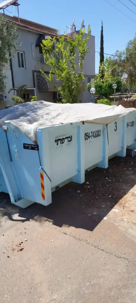 מכולת פסולת תכלת מכוסה ברשת מול בית פרטי