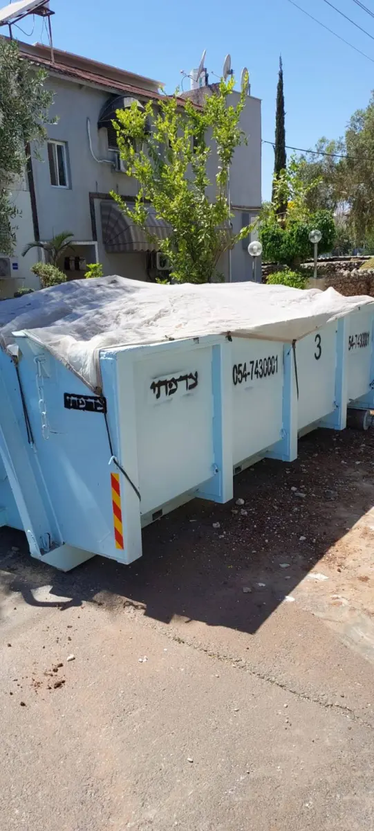 מכולת פסולת תכלת מכוסה ברשת מול בית פרטי