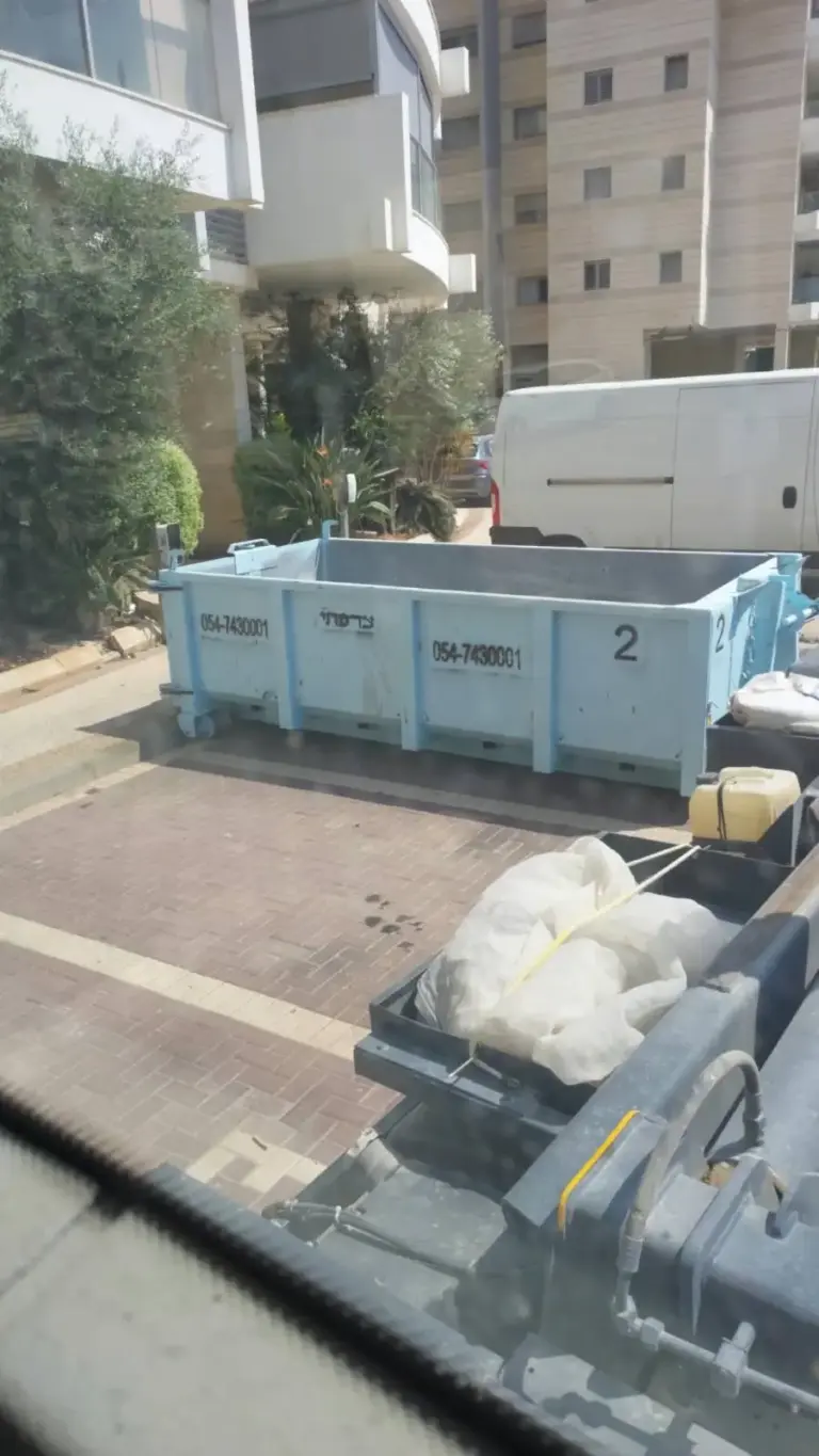 מכולת פסולת פתוחה ברחוב עירוני לצד בניין מגורים